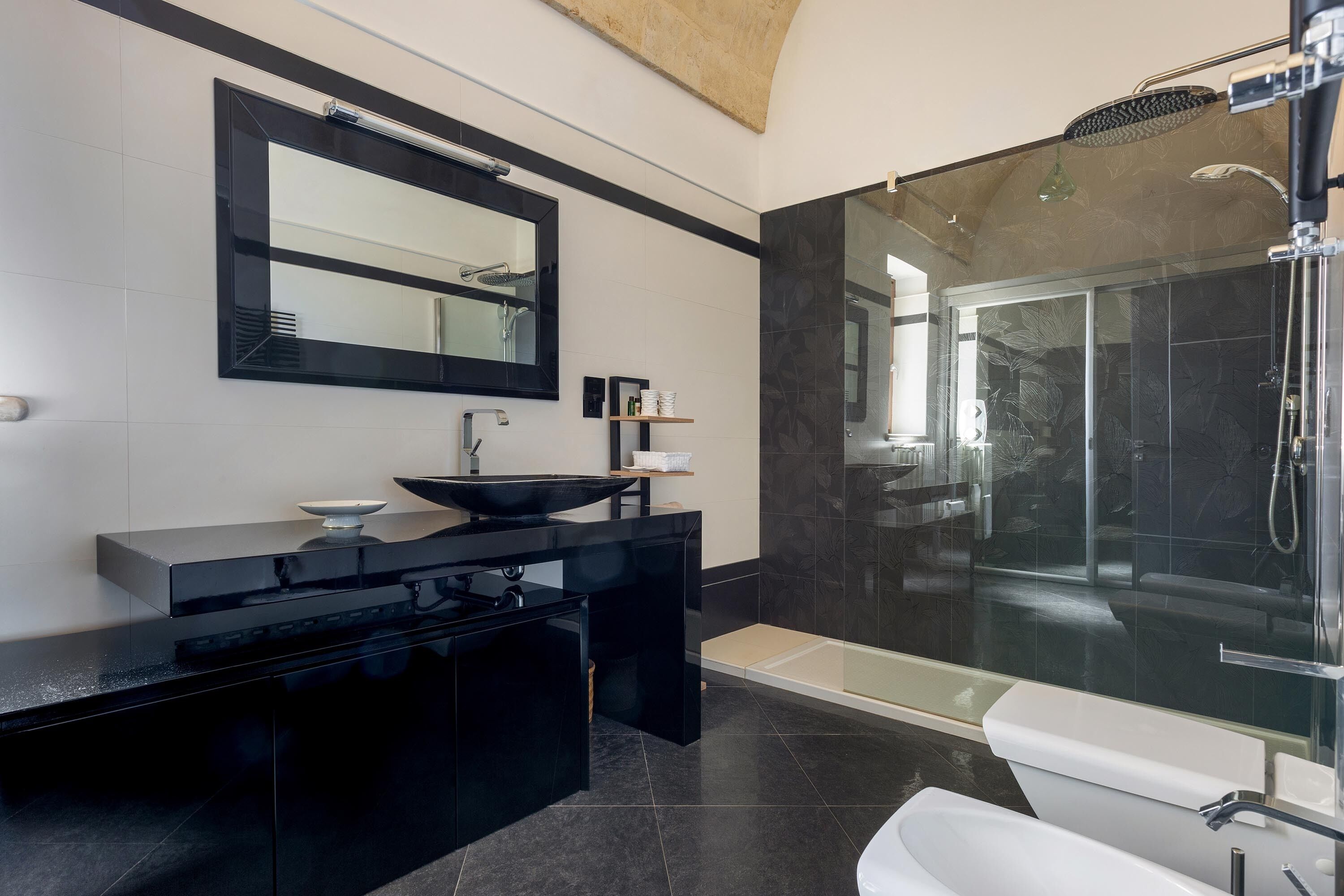 Un baño moderno con un mueble de tocador negro, un espejo grande, una ducha con cerramiento de vidrio y una bañera blanca.