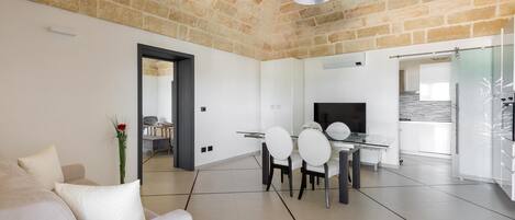 Una sala de estar moderna con techo de piedra, un comedor con mesa y sillas de vidrio, y un espejo grande que refleja el espacio.