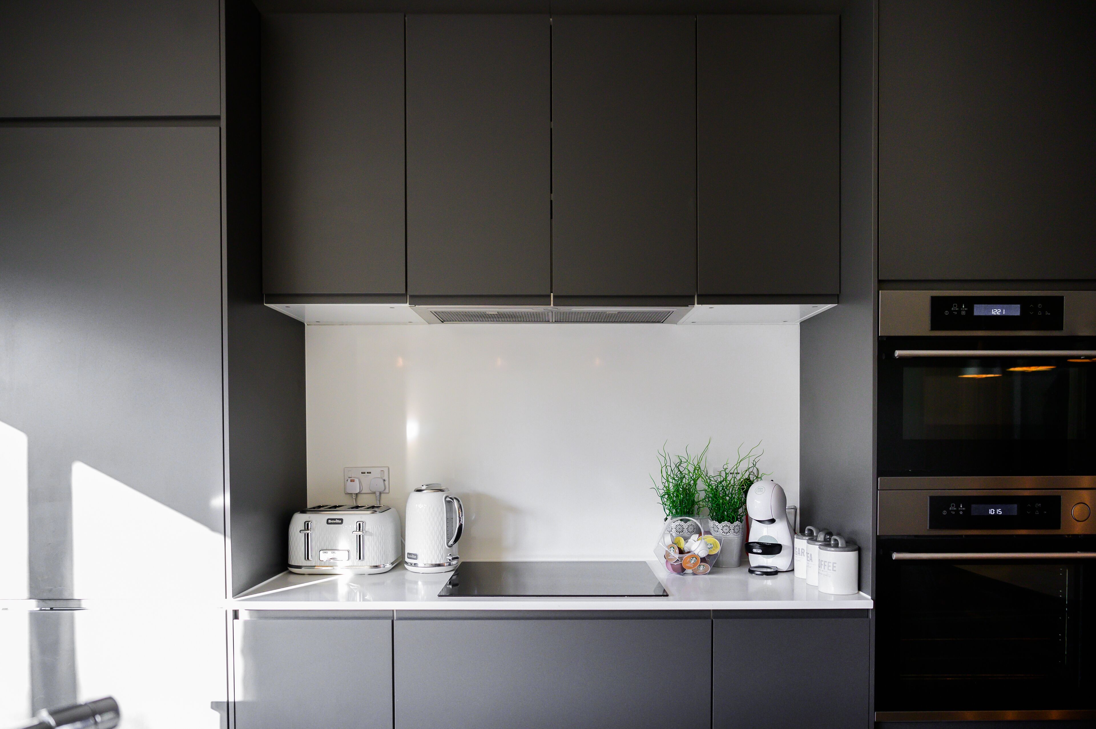 A modern kitchen with grey cabinets, a white countertop, a built-in oven, and a coffee maker.