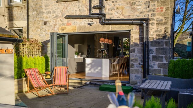Cocina de concepto abierto con comedor, fachada de piedra y zona de estar exterior con sillas a rayas.