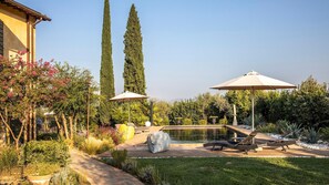 Ein gepflegter Garten mit Schwimmbad, Liegestühlen und Sonnenschirmen.