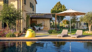 A poolside area with lounge chairs, a yellow bean bag, and a pergola with an umbrella. - Casale Santa Lucia 8 2 (Bettona)