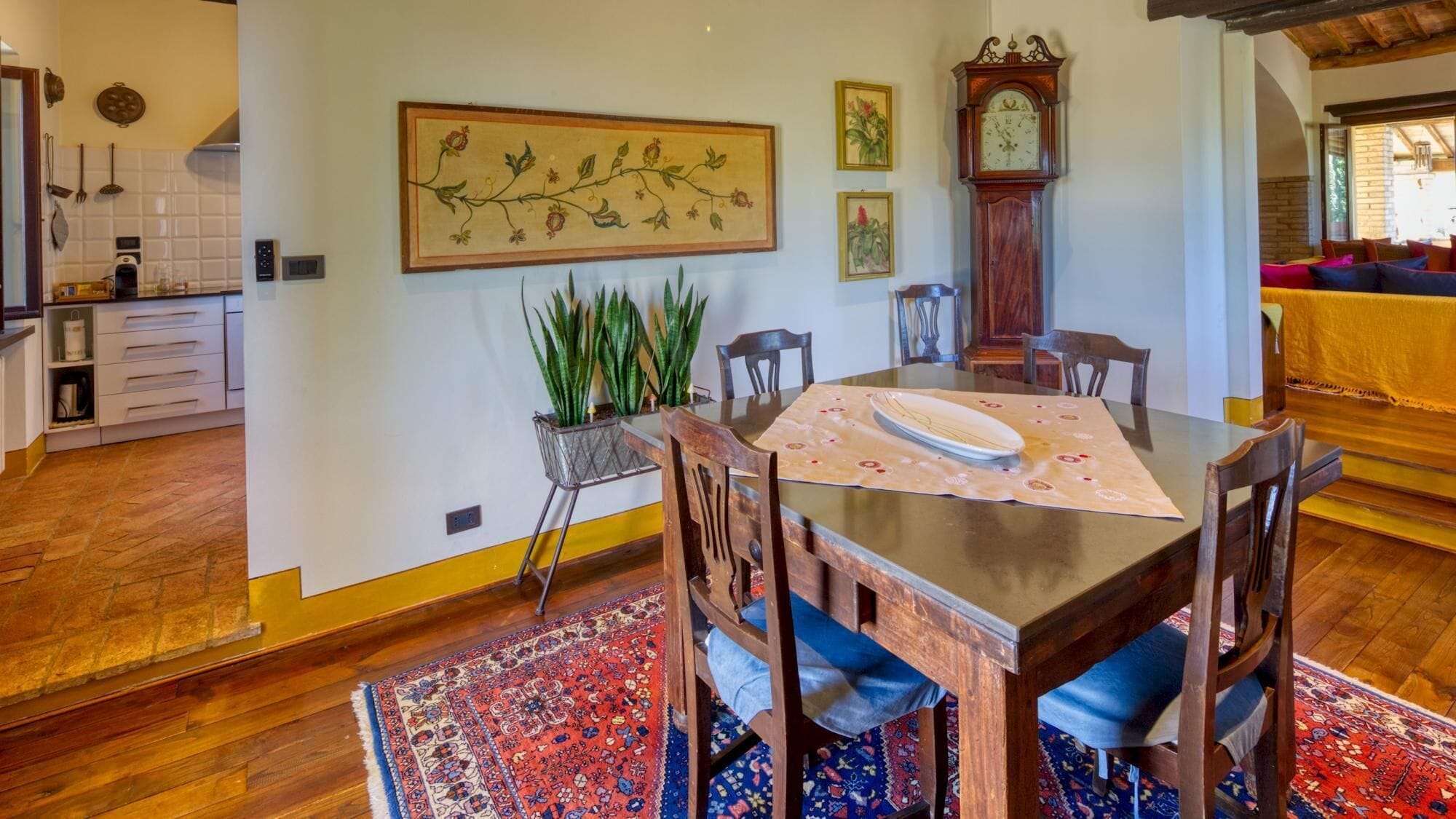 A dining area with a wooden table, chairs, a clock, and a plant.