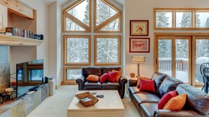 A cozy living room with a fireplace, leather sofas, a coffee table, and large windows offering a view of snow-covered trees. - Downtown WP Villa 491 I Great Views I Loft With Desk I Discounted Attractions (Winter Park)
