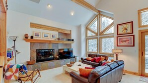 A cozy living room with a fireplace, a leather sofa, and a large window offering a view of trees. - Downtown WP Villa 491 I Great Views I Loft With Desk I Discounted Attractions (Winter Park)