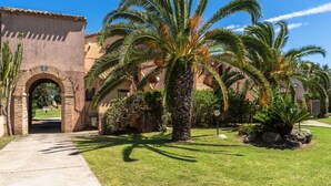 A courtyard with palm trees, a stone archway, and a building with a tiled roof. - Two-room apartment with 4 beds, (38 sq m): living room with kitchenette, table fridge and double sofa bed, double bedroom (beds can be separated), bathroom. <br>They can be on the ground floor with a patio or on the 1st floor with a balcony, both equippe (Pula)