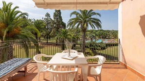 A balcony with a table and chairs, overlooking a pool and palm trees. - Two-room apartment with 4 beds, (38 sq m): living room with kitchenette, table fridge and double sofa bed, double bedroom (beds can be separated), bathroom. <br>They can be on the ground floor with a patio or on the 1st floor with a balcony, both equippe (Pula)