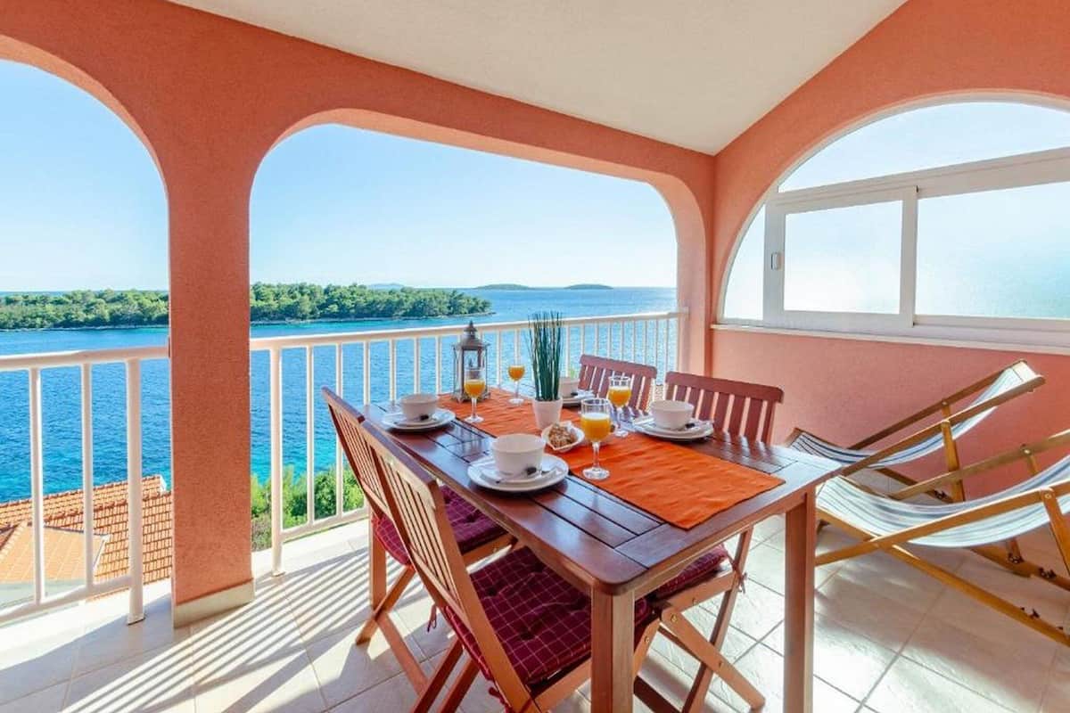 A dining area with a table set for two, overlooking a body of water and a distant landmass.