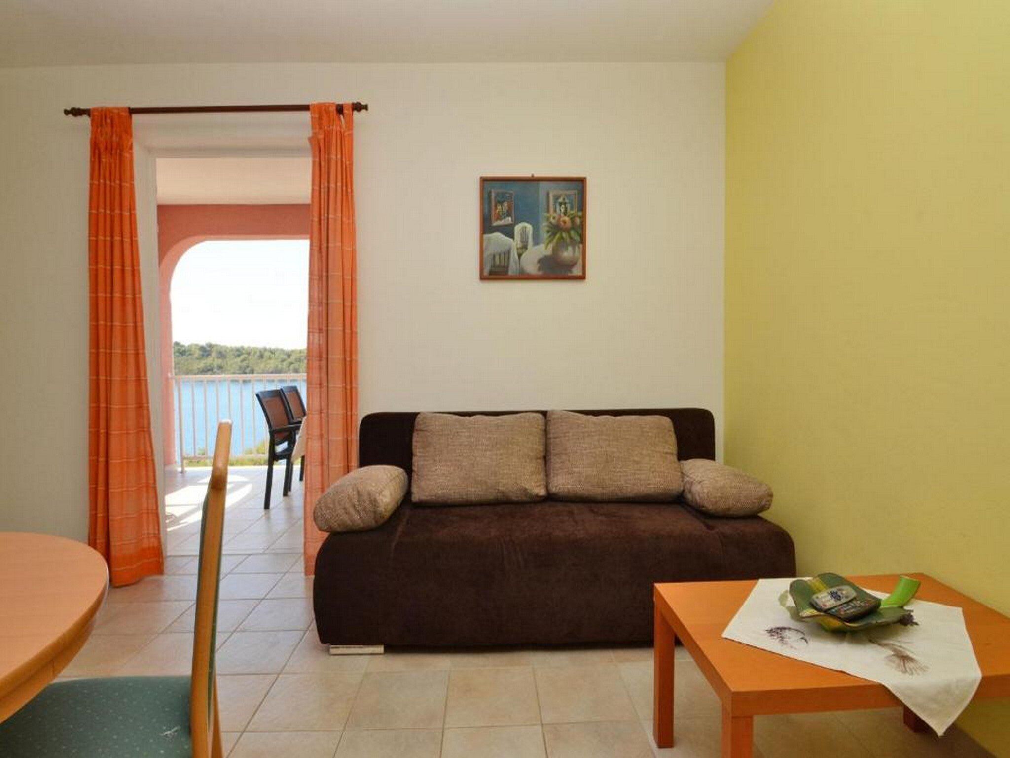 Una sala de estar con un sofá marrón, una mesita con un objeto verde y un cuadro en la pared.