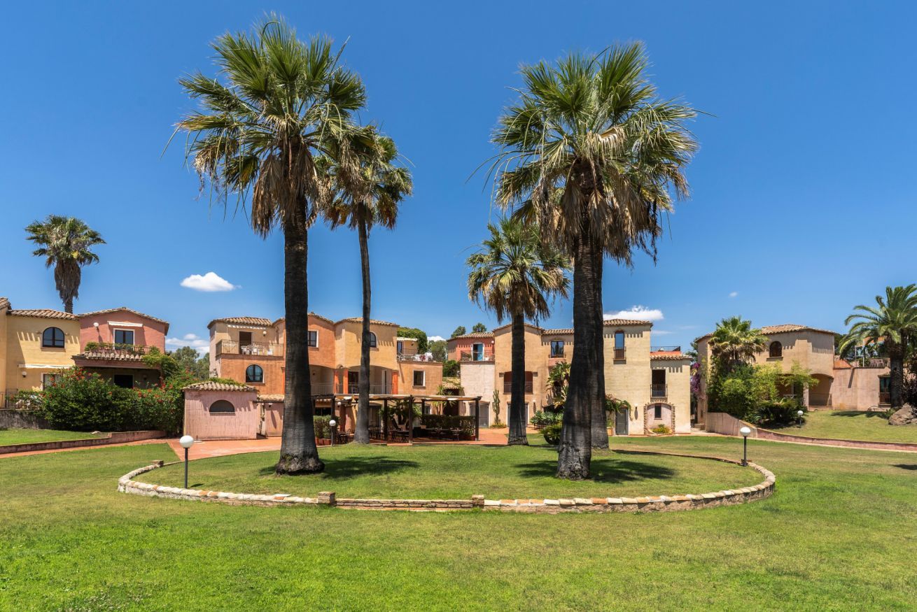 A courtyard with palm trees, a pool, and Mediterranean-style buildings.