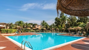Una piscina con sillones de descanso y sombrillas, rodeada de palmeras y edificios.