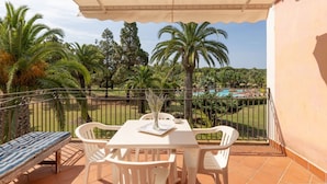 Un balcón con mesa y sillas, con vistas a una piscina y palmeras.