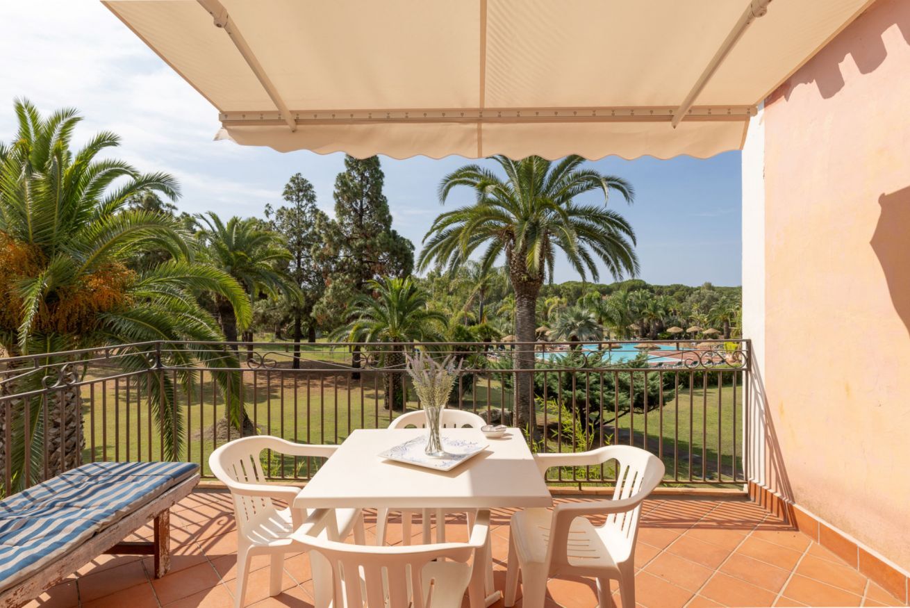 Un balcon avec une table et des chaises, donnant sur une piscine et des palmiers.
