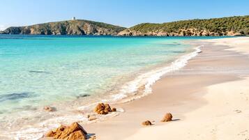 Une plage à l’eau turquoise et limpide, avec un rivage sablonneux et des affleurements rocheux.
