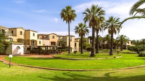A courtyard with palm trees, a pool, and a building with balconies. - Studio apartment 2 beds, (20/25 mq): living room with kitchenette, table fridge and double or double bed, bathroom. <br>All studios are located <b>on the ground floor</b>.<br>All the flats have a view of the park. <br>The apartments are equipped with: <b (Pula)