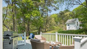 Eine Terrasse mit Korbmöbeln, einem Grill und einem kleinen Schuppen in einem bewaldeten Gebiet.
