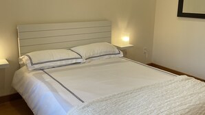 A neatly made bed with white linens and a headboard, two bedside lamps, and a wall-mounted mirror. - Stunning spacious suite with amazing views! (Halfmoon Bay)
