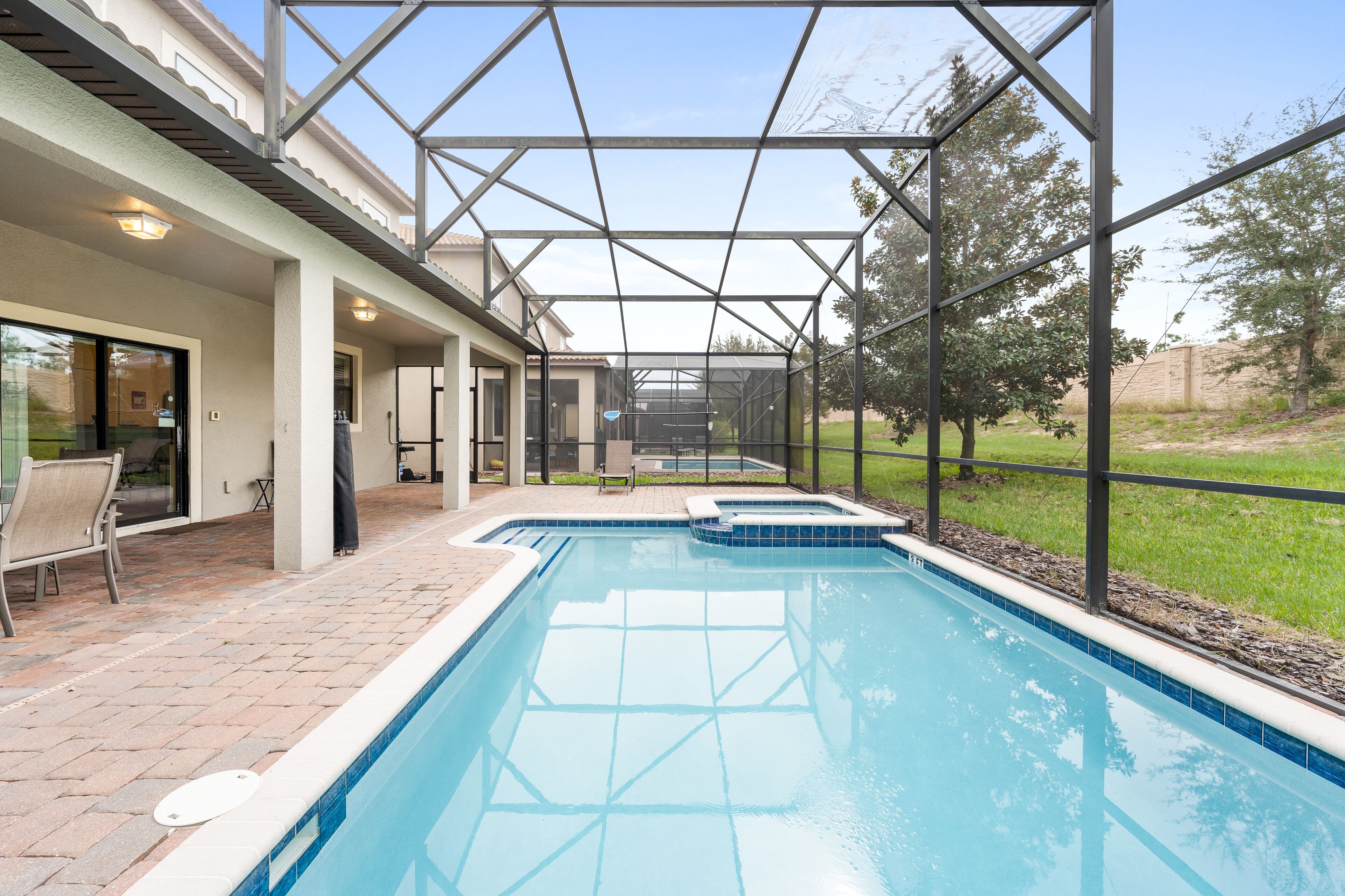 A swimming pool with a glass enclosure, a patio area with chairs, and a view of the surrounding landscape.