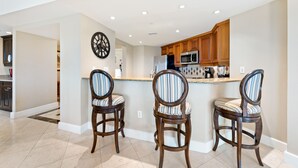 A modern kitchen with wooden cabinets, a stainless steel refrigerator, and two striped bar stools. - Luxury Condo with Amazing Views Near Attractions (Kissimmee)