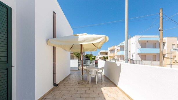 A balcony with a table and chairs, a white umbrella, and a view of neighboring buildings.