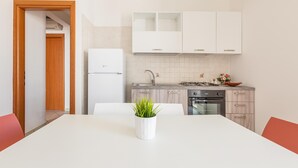 A modern kitchen with white cabinets, a white refrigerator, and a dining table with a potted plant.