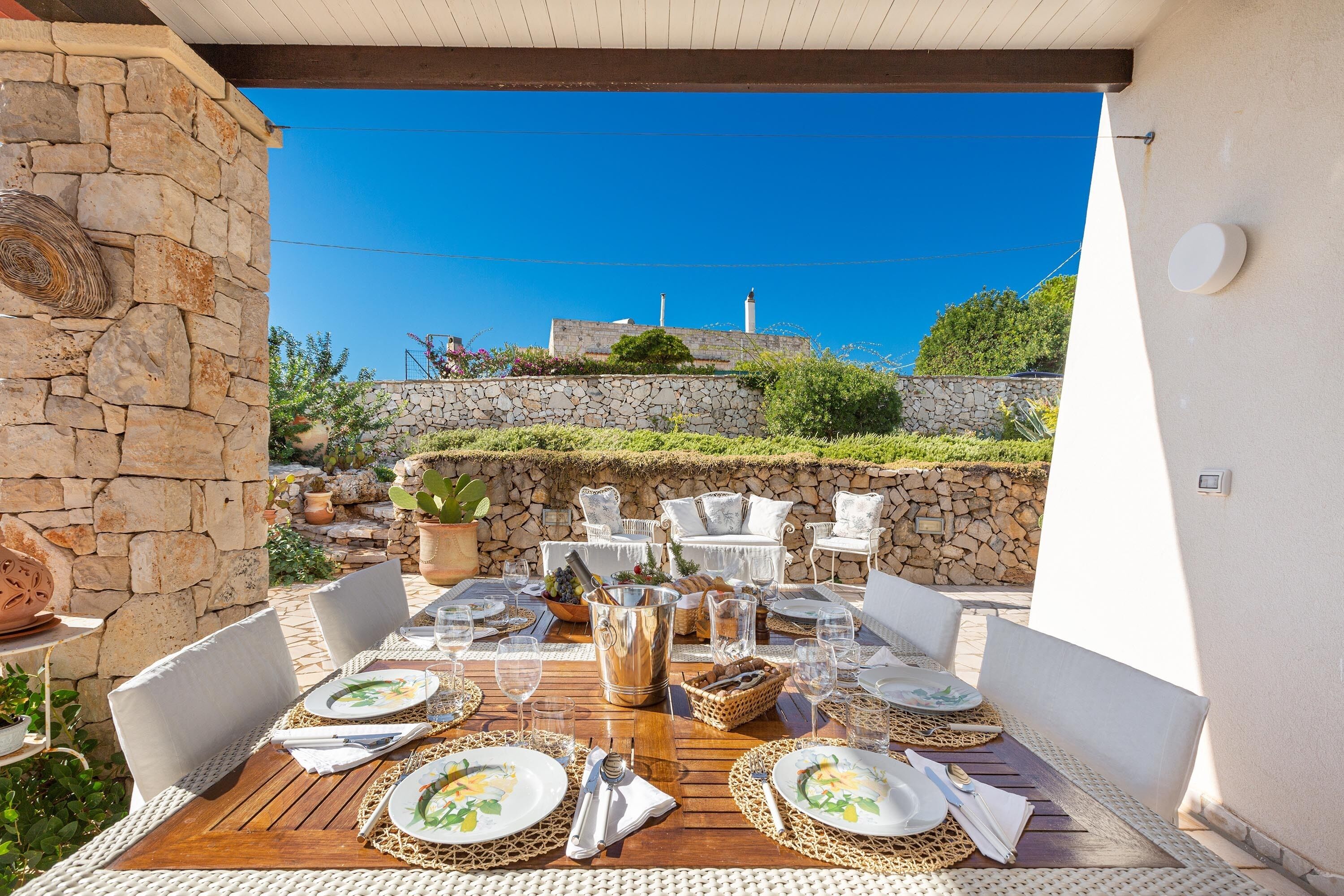 An outdoor dining area with stone walls, white furniture, and a clear view of the landscape.