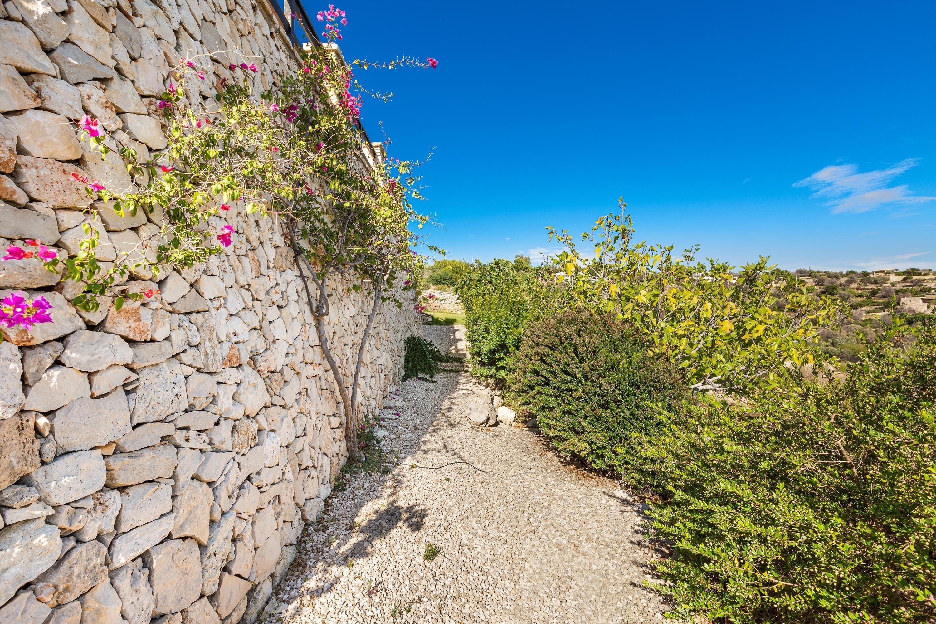 En sti af sten der fører til en stenvæg med lyserøde blomster.