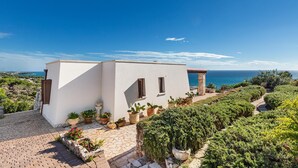 Un edificio moderno blanco con un sendero de piedra que conduce a una puerta, rodeado de plantas en macetas y vistas al mar.