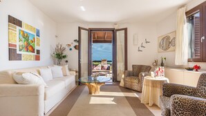 Un salón amplio con un sofá color beige, una mesa de centro de vidrio, sillones estampado de leopardo y vistas al exterior.