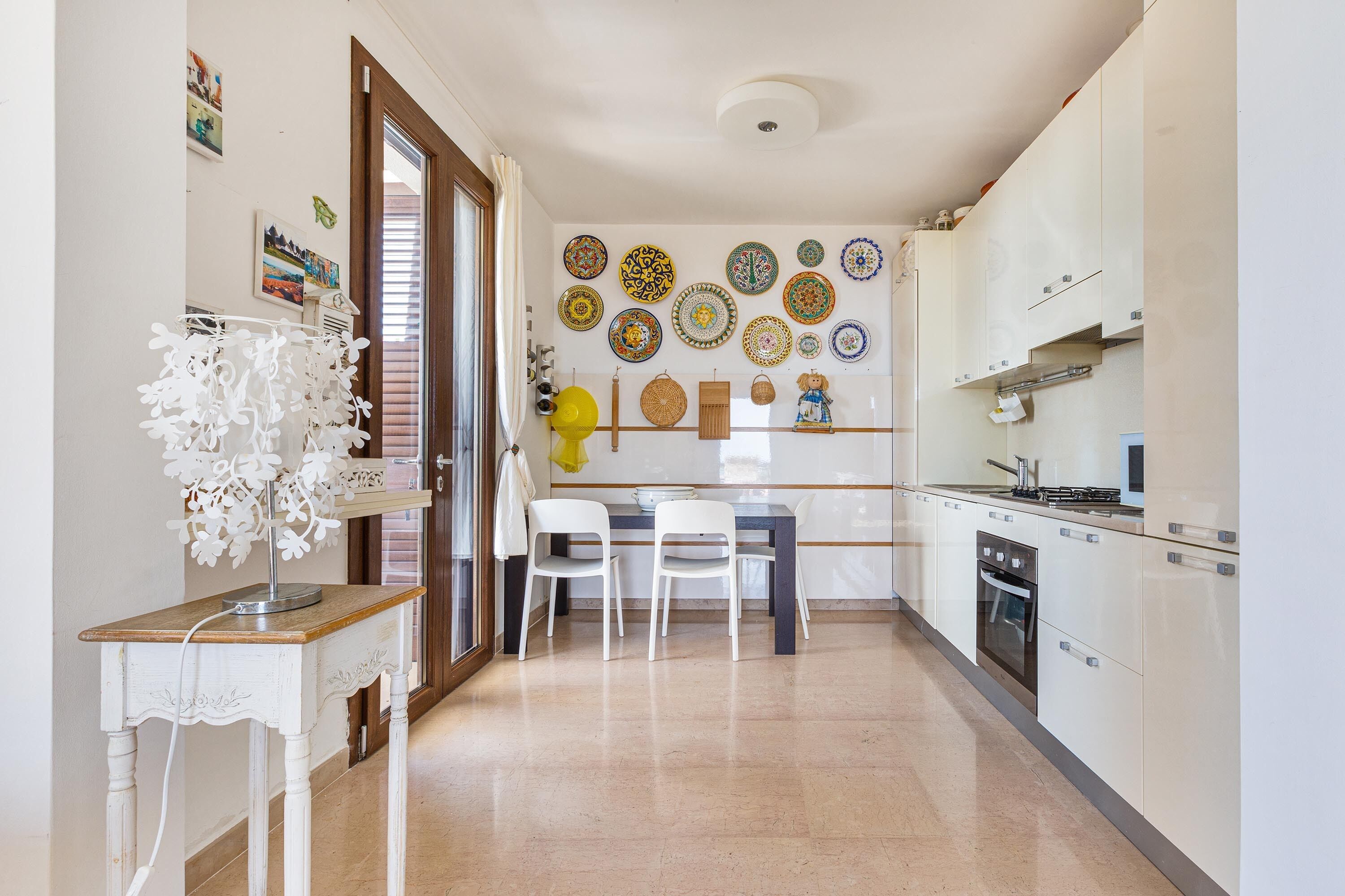 Een keuken met witte kastjes, een eettafel met stoelen en een wand versierd met borden.