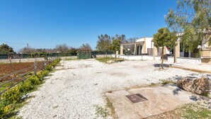 A building with a gravel driveway, a metal manhole cover, and a fenced area with greenery.