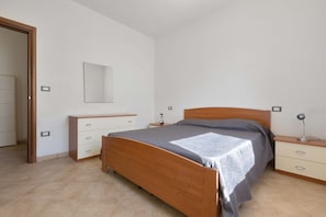 A bedroom with a wooden bed, a bedside table with a lamp, a dresser, and a mirror on the wall.