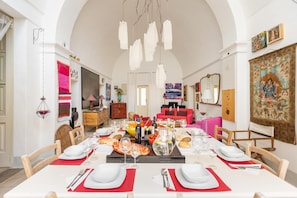 Uma sala de jantar com uma mesa comprida posta para refeição, rodeada por cadeiras de madeira.