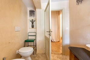 A compact bathroom with a toilet, a green chair, a door leading to a shower area, and a sink. - 2426 Dimora Santi Mancuso Appartamento by Barbarhouse (Presicce-Acquarica)
