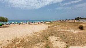 A beach with umbrellas and people, a clear sky, and a fence in the background.