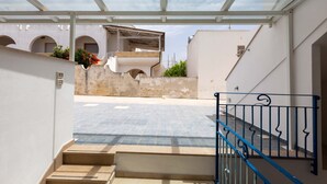 A covered outdoor area with a staircase leading to a building with a balcony.