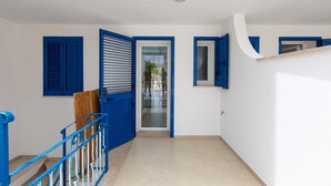 A hallway with blue shutters, a wooden door, and a staircase with blue railings.