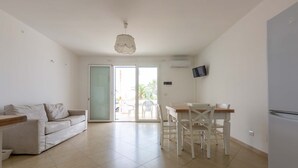 A spacious living area with a sofa, a dining table with chairs, a ceiling light, and a sliding glass door leading to an outdoor area.