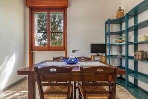 Uma área de refeições com uma mesa de madeira, quatro cadeiras, uma tigela azul, uma televisão e um móvel azul com objetos decorativos.
