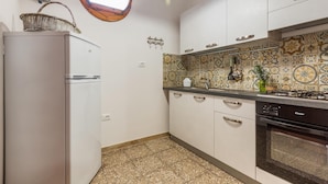 Une cuisine avec des armoires blanches, une cuisinière à gaz, un four encastré, un réfrigérateur, une fenêtre avec un cadre en bois et un crédence décorative en carreaux.