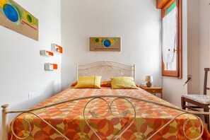 Quarto com cama, almofadas, mesa de cabeceira com abajur e uma cadeira.