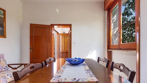 Une table à manger ornée d’un vase bleu au centre, entourée de chaises en bois, dans une pièce dotée d’une porte et d’une fenêtre en bois.