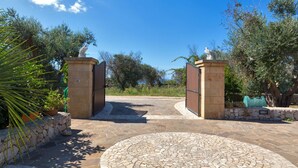 A stone pathway leading to a gated entrance with statues on pedestals, surrounded by olive trees and a clear sky. - 2518 Villa del Cavaliere by Barbarhouse (Castrignano del Capo)