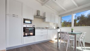A modern kitchen with white cabinetry, a built-in oven, microwave, and gas stove. There is a dining area with a glass table and white chairs. - 2518 Villa del Cavaliere by Barbarhouse (Castrignano del Capo)