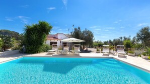 A clear blue pool with lounge chairs and umbrellas, surrounded by greenery and a building with a tiled roof. - 2518 Villa del Cavaliere by Barbarhouse (Castrignano del Capo)