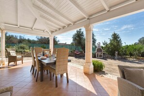 Eine Terrasse im Freien mit überdachter Essgegend, Korbmöbeln und einem gepflasterten Weg.