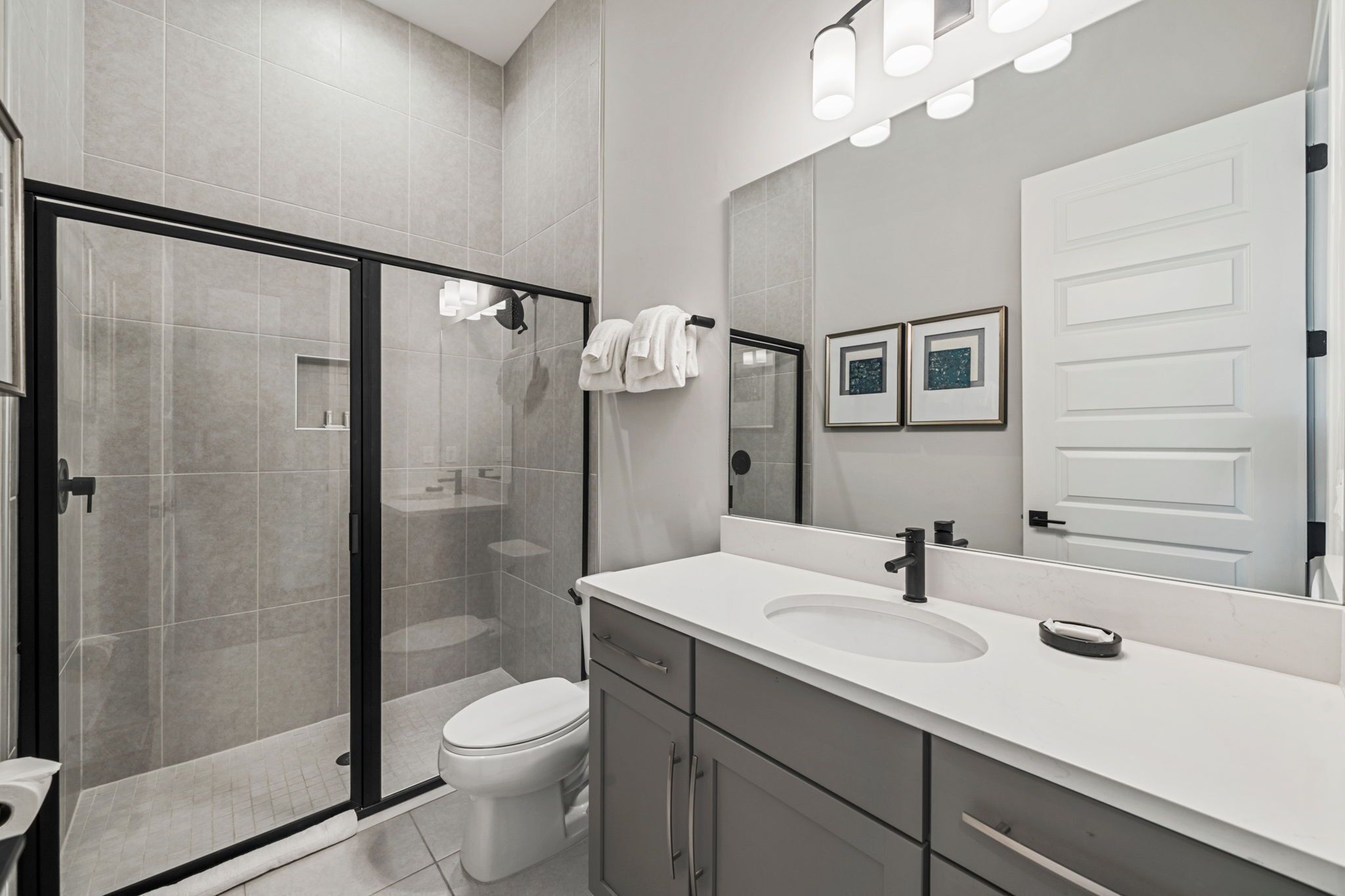 A modern bathroom with a glass-enclosed shower, a white sink, and a large mirror.