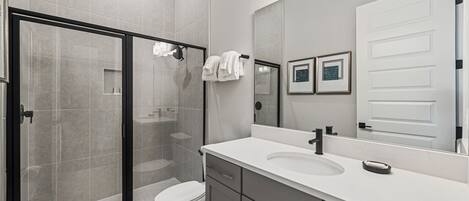 A modern bathroom with a glass-enclosed shower, a white sink, and a large mirror.