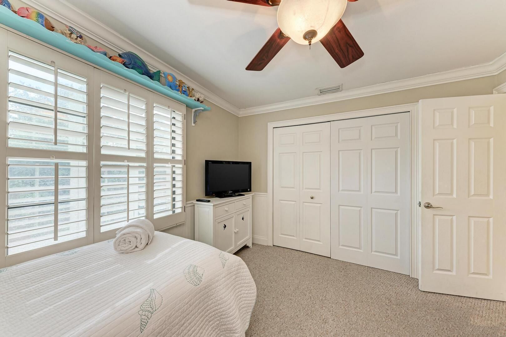 A bedroom with a bed, a television, a ceiling fan, and a wardrobe.