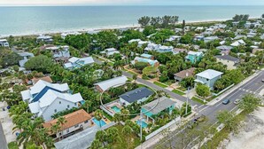 Vue aérienne d’un quartier résidentiel situé sur la côte, avec des maisons, une piscine et une plage en arrière-plan.
